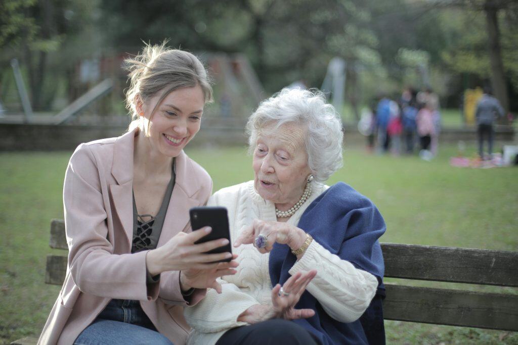 A younger woman and an older woman sharing a phone on a park bench